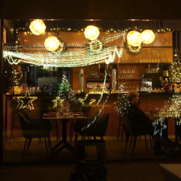Weihnachtlich dekoriertes Restaurant mit Lichtern und einem Gast, der an einem Tisch sitzt.