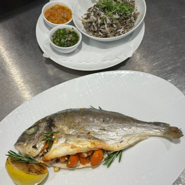 Gegrillter Fisch mit Gemüse und Kräutern, serviert mit Beilagen aus Reis und Saucen in Schalen.