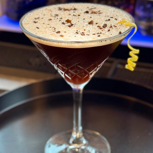 Dunkler Cocktail mit Schaum und Schokoladenstückchen, garniert mit einer Zitronenschale, auf einem Tisch im Adventure Park.