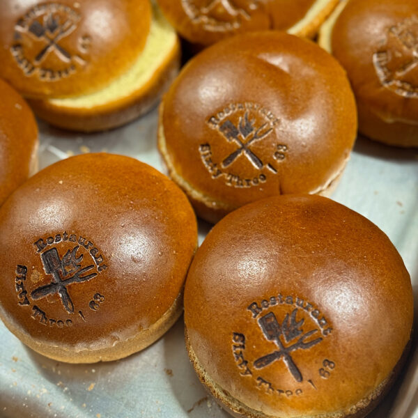 Sechs runde Brötchen mit eingestanztem Logo des Restaurants "Sixty Three" auf einer silbernen Platte.